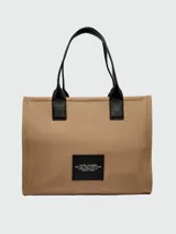 Bolso tipo tote Marc Jacobs modelo The Cargo Canvas Large Tote Bag, color tostado, confeccionado en lona con múltiples bolsillos delanteros con solapa y cierre, detalle de anilla metálica y estampado gráfico con el nombre de la marca. Cuenta con asas dobles para el hombro.