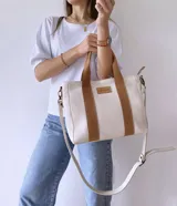 Bolso tipo tote de lona color crudo con detalles en cuero color marrón. Tiene doble asa corta de mano y correa larga de hombro.