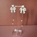 Par de aros colgantes con forma de lazo blanco y corazón, con cadena plateada y perlas colgantes.