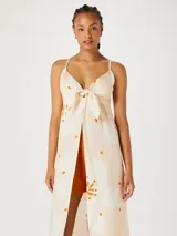 Musculosa tipo túnica de largo midi, con diseño estampado de flores en tonos claros y detalles en naranja. Presenta un escote en V con detalle de nudo frontal y breteles finos.