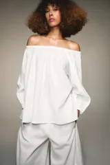 Blusa blanca de lino con escote recto y hombros descubiertos, manga abullonada tres cuartos terminada en elástico.