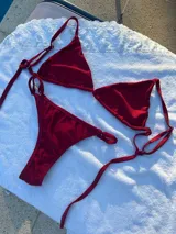 Conjunto de bikini rojo brillante, compuesto por un corpiño triangular con tirantes finos y una tanga con tirantes laterales ajustables.