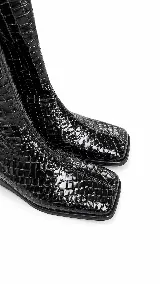Bota de caña media con punta cuadrada y cierre lateral, confeccionada en cuero con textura croco y acabado charol negro.