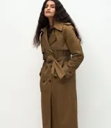 Trench coat largo de Marfinno, confeccionado en gabardina de poliéster. Presenta cuello con solapas, aletas en los hombros, cierre frontal con botones y cinta para lazo en la cintura.