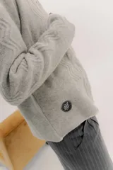 Saco tejido de lana con diseño de ochos y aranes en el frente. Presenta cierre frontal con ganchos peleteros, cuello redondo y pin bordado de la marca en la parte inferior.