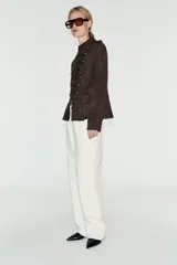 Chaqueta de gamuza marrón con cuello alto, manga larga y bajo con peplum. Cuenta con doble botonadura decorativa de botones metálicos dorados en el frente y cierre con ganchos ocultos.