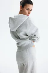 Campera canguro de felpa color gris melange, de corte holgado con interior cepillado suave. Cuenta con hombros caídos, capucha forrada, cierre frontal y bolsillos delanteros abiertos, con puños y bajo en punto acanalado.