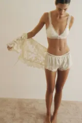 Bombacha tipo shortie de tiro alto, color crema o blanco roto, confeccionada en microfibra lisa con un amplio ribete de encaje floral en el ruedo inferior.