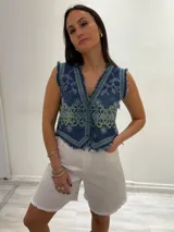 Chaleco corto en denim azul con detalle desflecado y bordado artesanal en tonos celeste y dorado. Estilo boho chic con escote en V, ideal para combinar con prendas básicas y elevar tu look.