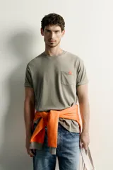 Camiseta verde militar de corte regular, con cuello redondo, manga corta y un bolsillo de parche en el pecho con etiqueta decorativa contrastante.