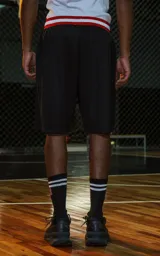 Bermuda deportiva negra de estilo NBA, confeccionada en tejido de punto deportivo. Presenta un elástico en la cintura con franjas rojas y blancas. Estampado frontal con la palabra "RAVERS" y el número "90" en rojo con borde blanco.