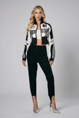 Campera corta con cierre frontal, confeccionada en una combinación de tela y apliques de cuerina, con diseño bicolor en blanco y negro, cuello alto y estampas de estilo motociclista.