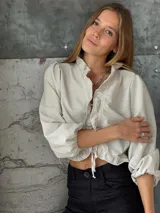 Blusa negra de lino con acabado brillante, de manga larga abullonada, escote con volados y cierre frontal con tiras para anudar.