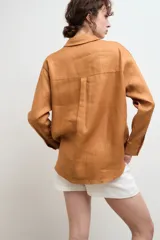 Camisa oversize de lino, color tostado, con cuello clásico, cierre frontal de botones y bolsillo en el pecho.
