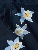 Remera de algodón Tommy Hilfiger en color azul marino, con cuello redondo y mangas cortas. Presenta un delicado diseño bordado de flores alrededor del escote y el pequeño logo de la bandera de la marca en la manga.