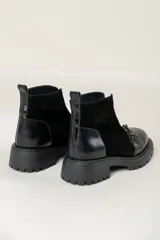 Bota corta de cuero negro con suela track, cierre frontal con cremallera y tira decorativa con hebilla metálica sobre el empeine.