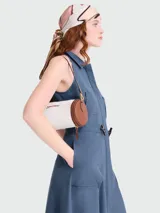 Bolso tipo shoulder bag de Longchamp, modelo Épure Surf XS. Diseño cilíndrico en color blanco con detalles en cuero marrón en los extremos y cierre de cremallera. Incluye correa fina de hombro y el logotipo de la marca impreso en el lateral.