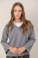 Campera de punto gris con cierre frontal completo, cuello redondo y mangas anchas. Presenta un detalle de tirador de cuero en el cierre.