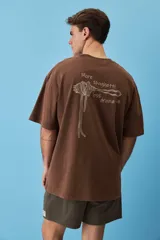 Remera marrón oversize de manga corta, con cuello redondo y pequeño estampado gráfico en el pecho.