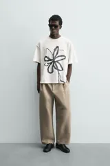 Camiseta de corte relajado confeccionada en algodón, con cuello redondo y manga corta. Presenta un estampado artístico de una flor a trazo grueso en color negro sobre fondo blanco.