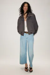 Chaqueta estilo bomber de color gris oscuro, con cuello subido, manga larga y corte holgado. Presenta bolsillos delanteros con solapa, bajo con pliegues y cierre frontal con cremallera oculta y botones a presión.