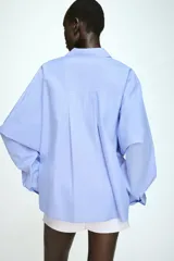 Camisa de manga larga en tejido de popelín color celeste, con cuello solapa, cierre frontal con botones y detalle de pliegue en el bajo.