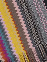 Chal tipo bufanda de punto con diseño de zigzag multicolor, característico de Missoni. Presenta un borde rojo sólido y flecos en los extremos.
