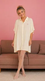 Camisa tipo vestido de corte holgado, confeccionada en viscosa suave, con cuello camisero, cierre frontal de botones, mangas cortas con dobladillo y bolsillos laterales. Presenta un pequeño bordado de corazón en el pecho.