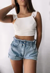 Short de jean celeste de tiro alto con cintura fruncida elástica y cierre frontal con dos botones metálicos. Presenta bolsillos delanteros y dobladillos anchos en los bordes.