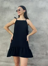 Vestido corto negro con textura de lunares, breteles finos con lazo y falda con volados.
