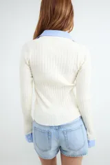 Cárdigan de punto color marfil con diseño de doble capa que incluye cuello polo y puños camiseros en tono celeste a rayas. Cuenta con cierre frontal de botones.