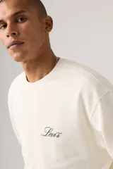 Buzo de cuello redondo Levi's de color marfil, con diseño relajado, mangas largas y pequeño logo cursivo bordado en el pecho.