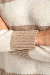 Sweater de punto con diseño de rayas horizontales anchas, alternando color beige camel y blanco roto con motas de color. Presenta cuello redondo y puños y borde inferior acanalados.