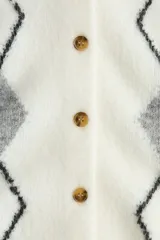 Saco corto de punto jacquard, color blanco con estampado de rombos en gris. Presenta cuello redondo, cierre frontal con botones y terminaciones acanaladas en puños y bajo.