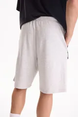 Bermuda de felpa sin friza de color negro, con cintura elastizada, cordón ajustable y bolsillos laterales con cierre. Presenta un pequeño logo estampado en el borde inferior.