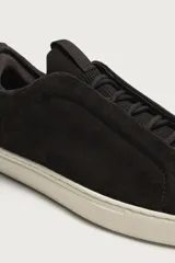 Zapatilla urbana de hombre confeccionada en piel con acabado de serraje, diseño minimalista sin cordones visibles y suela de goma a contraste.