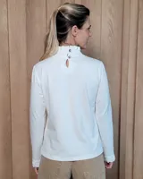 Polera de manga larga color blanco, confeccionada en algodón, con cuello alto tipo tortuga y detalles de volados en el cuello y en los puños.