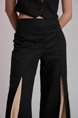 Pantalón largo color marrón, de corte ancho y tiro alto, con aberturas frontales en las piernas que revelan paneles internos en tono celeste.