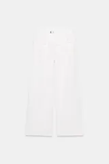 Pantalón blanco de nylon, tiro alto, con cintura elástica y detalle de sobrefalda o peplum superpuesto con hebilla metálica. Corte ancho y pierna recta.