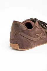 Zapatilla de estilo urbano confeccionada en cuero legítimo y gamuza en tono marrón, con diseño de costuras decorativas laterales y suela plana de goma.