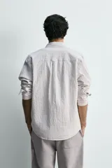 Camisa de corte relajado confeccionada en tejido de algodón con textura, diseño a rayas verticales, cuello abotonado, manga larga con puños y bolsillo de plastrón en el pecho.
