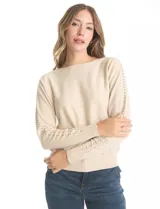 Buzo tejido color beige de manga japonesa, con detalle de tachas metálicas a lo largo de las mangas. Presenta puños y ruedo acanalados.