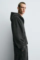 Sudadera con capucha y cierre de cremallera, de corte relajado (relaxed fit), confeccionada en algodón con interior afelpado. Presenta bolsillos frontales tipo canguro y acabados en rib. El tejido tiene un efecto lavado que le da un color negro desgastado.