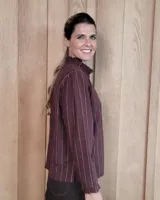 Camisa de algodón a rayas verticales blancas y azules, con cuello alto tipo gorguera con volados, cierre frontal de botones y mangas largas con puños con volados.
