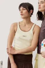 Musculosa de tejido rib color beige con detalles marrones en los bordes del cuello y sisas. Cuenta con el logotipo de la marca bordado en el pecho.