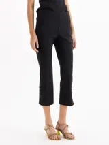 Pantalón negro de tiro alto y calce ajustado, con recortes centrales y tajos en los laterales del ruedo decorados con pequeños moños satinados.