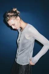 Chaqueta gris de punto fino semitransparente con hilo metalizado, cuello redondo, manga larga y cierre frontal con botones.