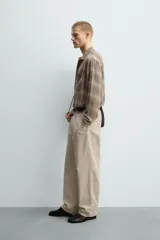 Camisa relaxed fit de manga larga con cuello solapa, confeccionada en tejido con mezcla de viscosa. Presenta un bolsillo plastrón en el pecho, bajo con aberturas laterales y cierre frontal de botonadura. El diseño es a cuadros en tonos beige y marrón.