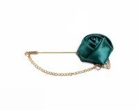 Pin para el ojal con diseño de flor de tela satinada en color verde esmeralda, montado sobre un alfiler metálico dorado con cadena decorativa.