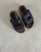 Sandalia tipo birkenstock de cuero negro, con dos tiras ajustables con velcro y plantilla anatómica marrón.